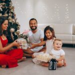 Happy family opening Christmas gifts by the decorated tree indoors.