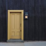 A modern yellow door on a dark wooden facade creates a striking contrast. Architectural detail.