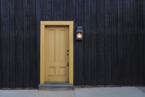A modern yellow door on a dark wooden facade creates a striking contrast. Architectural detail.