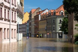 Street flooding in a European city with historic architecture under a sunny sky.