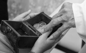 A touching black and white image of hands exchanging coins in a small wooden box, symbolizing trust and tradition.