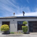 A worker installs solar panels on a house roof under a clear blue sky, showcasing renewable energy adoption.
