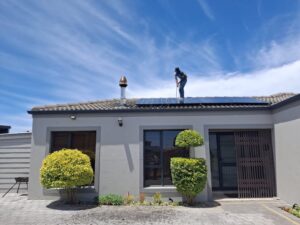 A worker installs solar panels on a house roof under a clear blue sky, showcasing renewable energy adoption.
