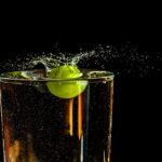 A grape makes a vibrant splash in a clear glass of water against a dark background.