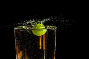 A grape makes a vibrant splash in a clear glass of water against a dark background.