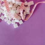 White sugar cubes with a pink tape measure on a purple surface, symbolizing diet awareness.