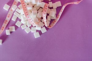 White sugar cubes with a pink tape measure on a purple surface, symbolizing diet awareness.