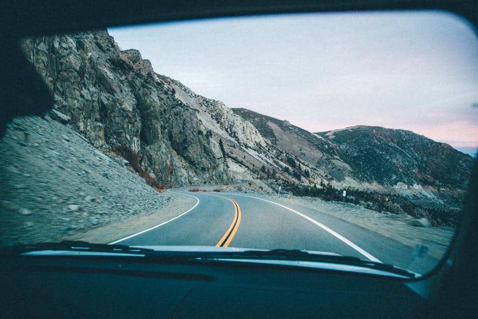 View of a winding mountain road through a car windshield during a road trip.