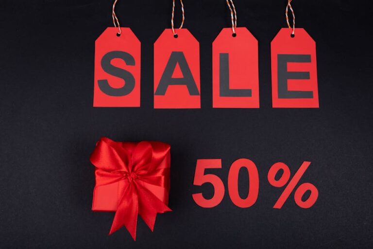 Red gift box next to sale tags and 50% sign on black background, ideal for promotions.
