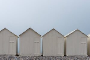 Minimalist image of white beach huts in a row against a clear sky, creating a serene coastal scene.