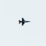 High-altitude jet fighter performing aerial maneuvers against a clear sky backdrop.