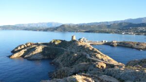 Stunning daytime aerial view of L'Île-Rousse's rugged coastline and hills in sunny Corsica, France.