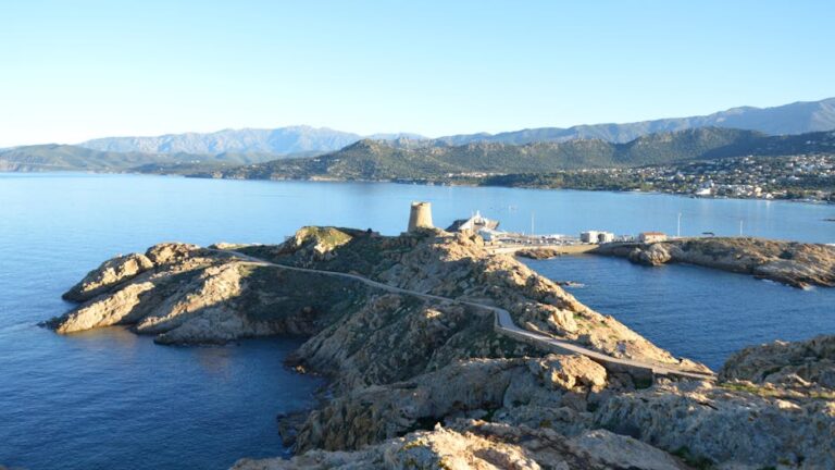 Stunning daytime aerial view of L'Île-Rousse's rugged coastline and hills in sunny Corsica, France.