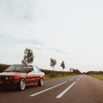 A classic red BMW sedan parked on a scenic countryside road during daylight.