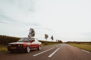 A classic red BMW sedan parked on a scenic countryside road during daylight.
