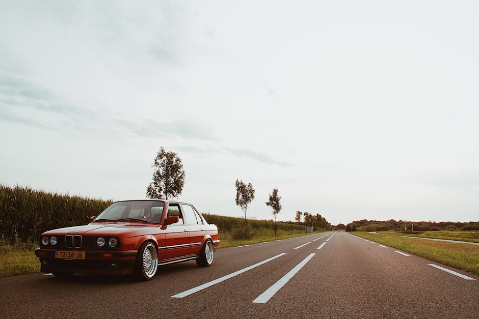 A classic red BMW sedan parked on a scenic countryside road during daylight.