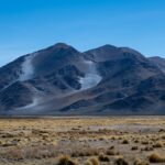 Serene mountain landscape with rugged peaks and sparse vegetation under a clear blue sky.