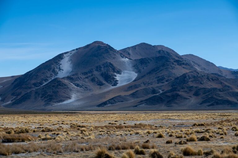 Serene mountain landscape with rugged peaks and sparse vegetation under a clear blue sky.