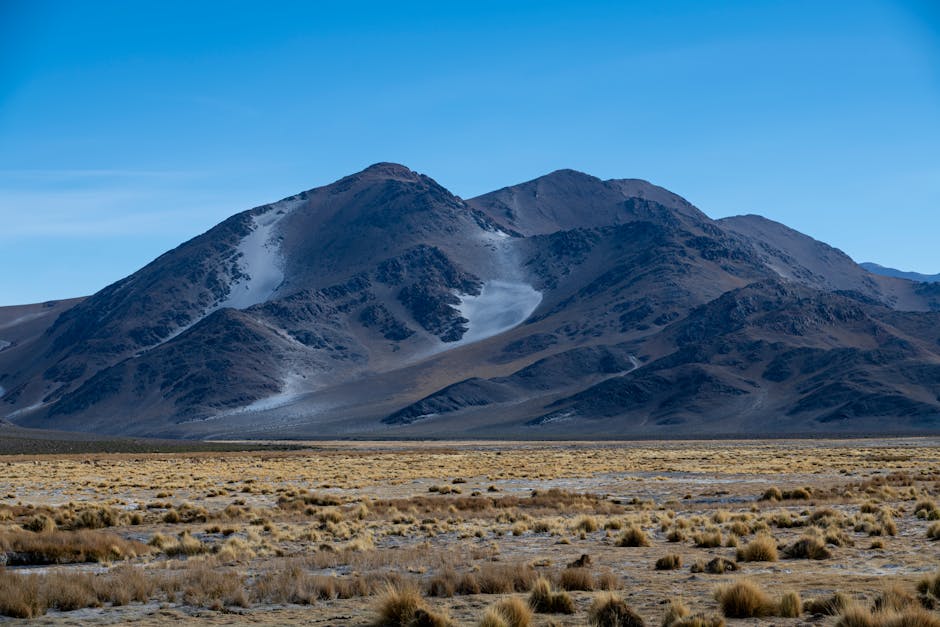 Serene mountain landscape with rugged peaks and sparse vegetation under a clear blue sky.