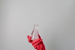 A hand in a red glove holding a laboratory flask against a neutral background.