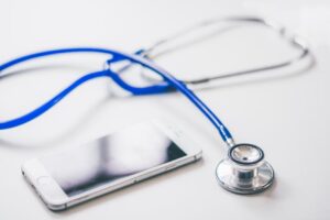 A smartphone and blue stethoscope on a clean white surface, emphasizing modern healthcare.