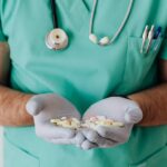 A healthcare professional in uniform holding a variety of pills in gloved hands.