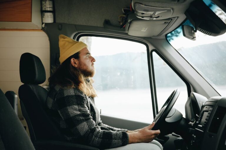 A young man in a beanie drives a campervan, capturing a candid travel moment.