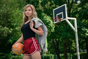 Athletic woman holding a ball while standing on an outdoor basketball court with a smile.