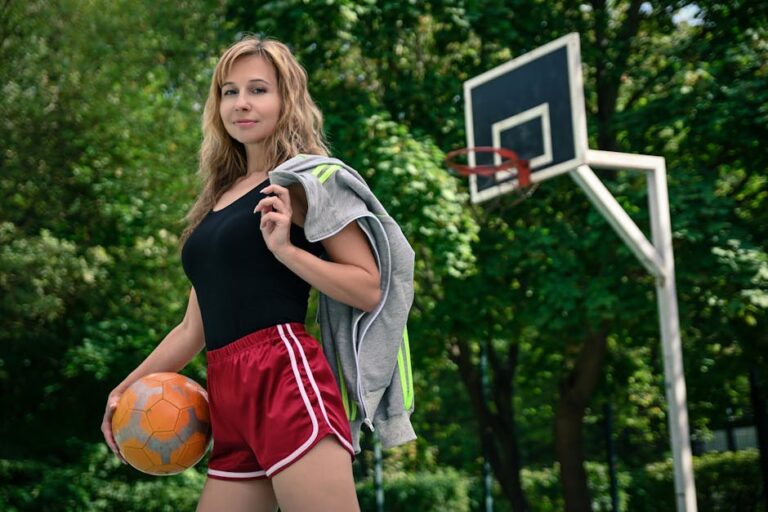 Athletic woman holding a ball while standing on an outdoor basketball court with a smile.
