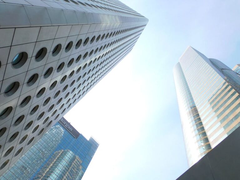 From below of tall tower with round windows located in Hong Kong city near various skyscrapers with glass mirrored facades against cloudless blue sky