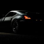 A dramatic shot of a Nissan 370Z sports car illuminated in darkness with vibrant tail lights.