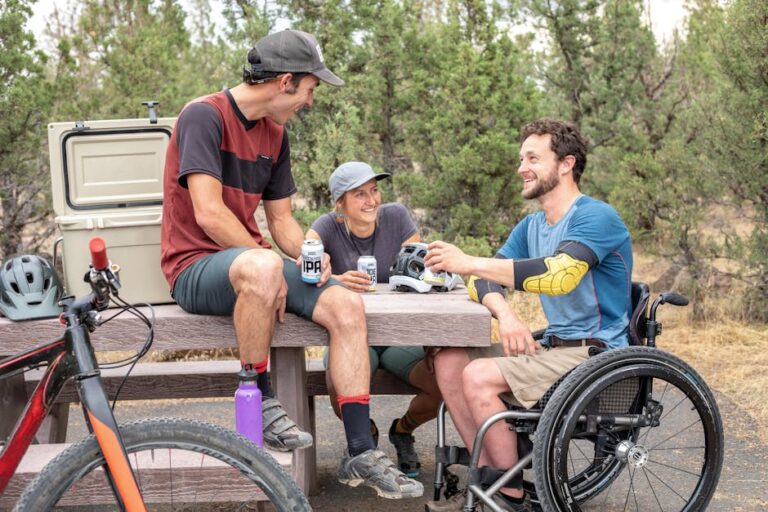 Group of friends having fun outdoors, chatting and enjoying drinks by a picnic table.