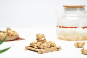 Close-up of organic ginger roots and herbal tea in a glass teapot on a white background.