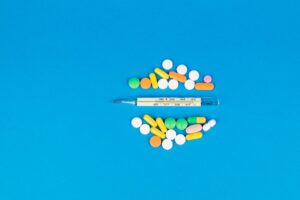 Top view of assorted colorful pills and a thermometer on a vibrant blue background.