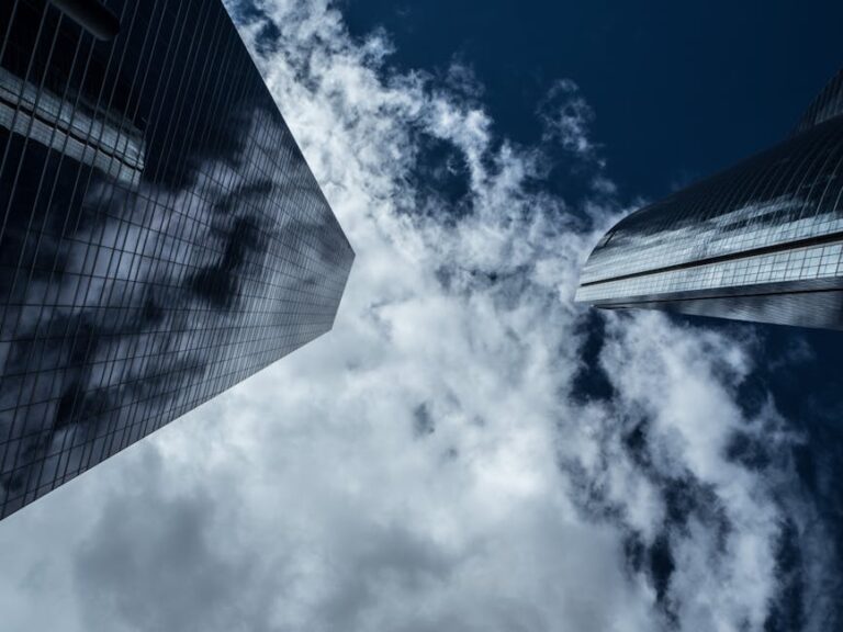 A low-angle shot of modern skyscrapers with reflections in glass windows against a cloudy sky.